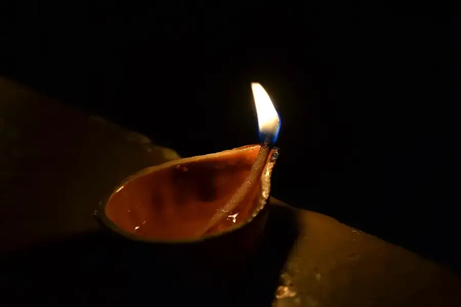 A small clay oil lamp with a single flame against a dark background